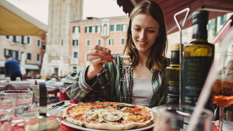 woman sprinkling cheese on pizza